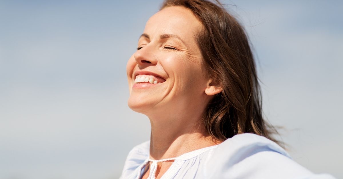 Smiling mature woman with closed eyes enjoying the sunshine, symbolizing peace, renewal, and self-empowerment.
