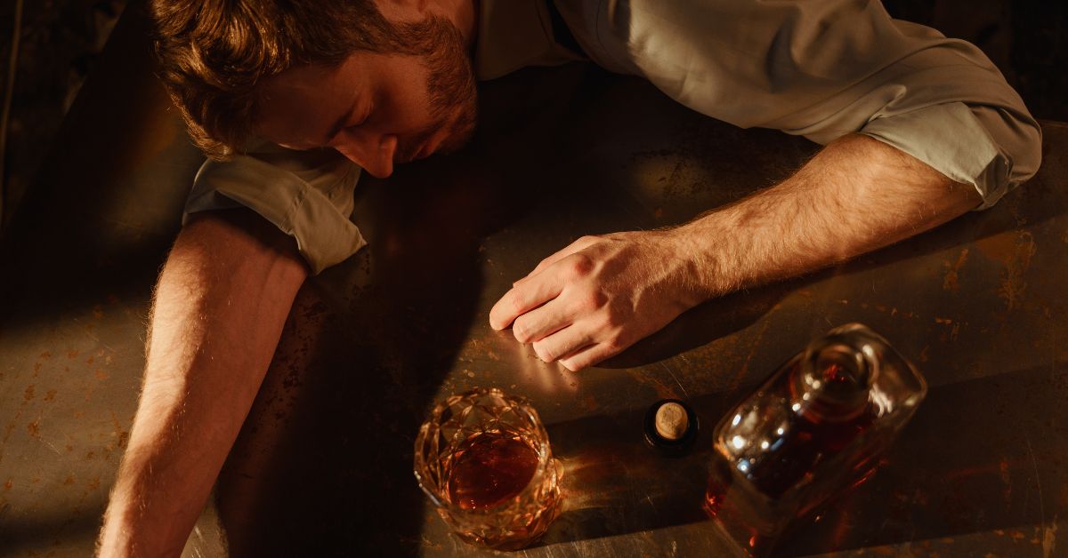Man passed out at a bar table with whiskey and an empty glass after heavy drinking.