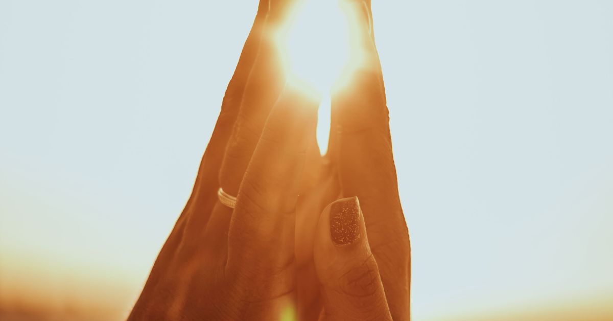 Close-up of two hands gently touching with sunlight shining through, symbolizing love, connection, and spiritual or soulmate bond.