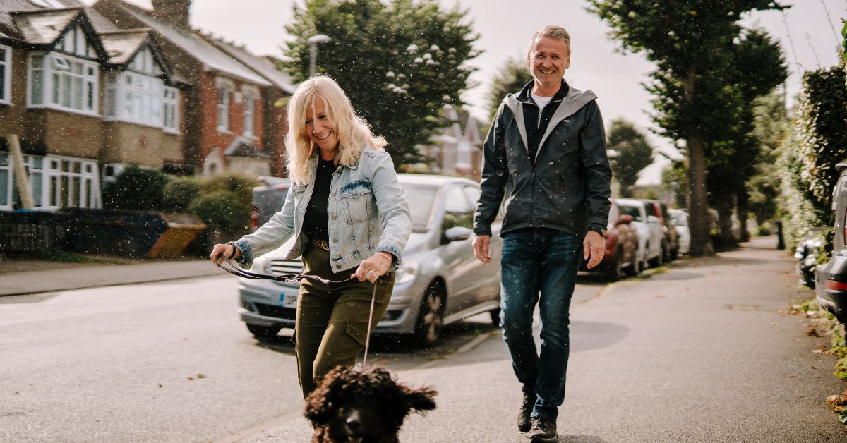 Happy mature couple walking a dog on a neighborhood street, enjoying shared outdoor activities.