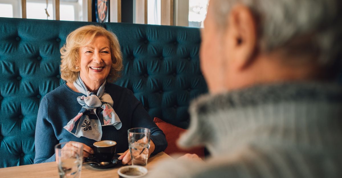 Smiling senior woman on a coffee date with a man, enjoying conversation and connection in a cozy café setting.
