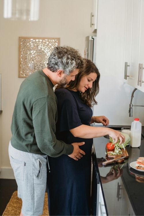 Middle-aged couple cooking together in a modern kitchen, preparing fresh vegetables and sandwiches on the counter.