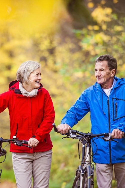 Mature couple walking their bicycles through a scenic autumn park, smiling and enjoying each other's company on a casual outdoor date.