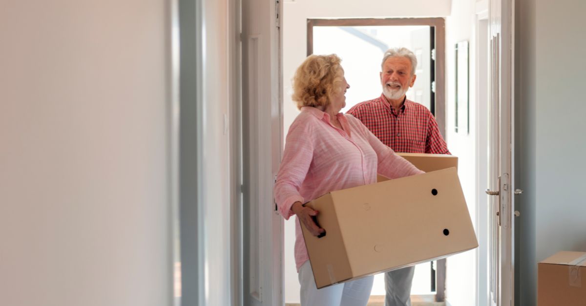 Smiling mature couple carrying cardboard boxes into a new home, symbolizing moving in together and starting a new chapter in life.