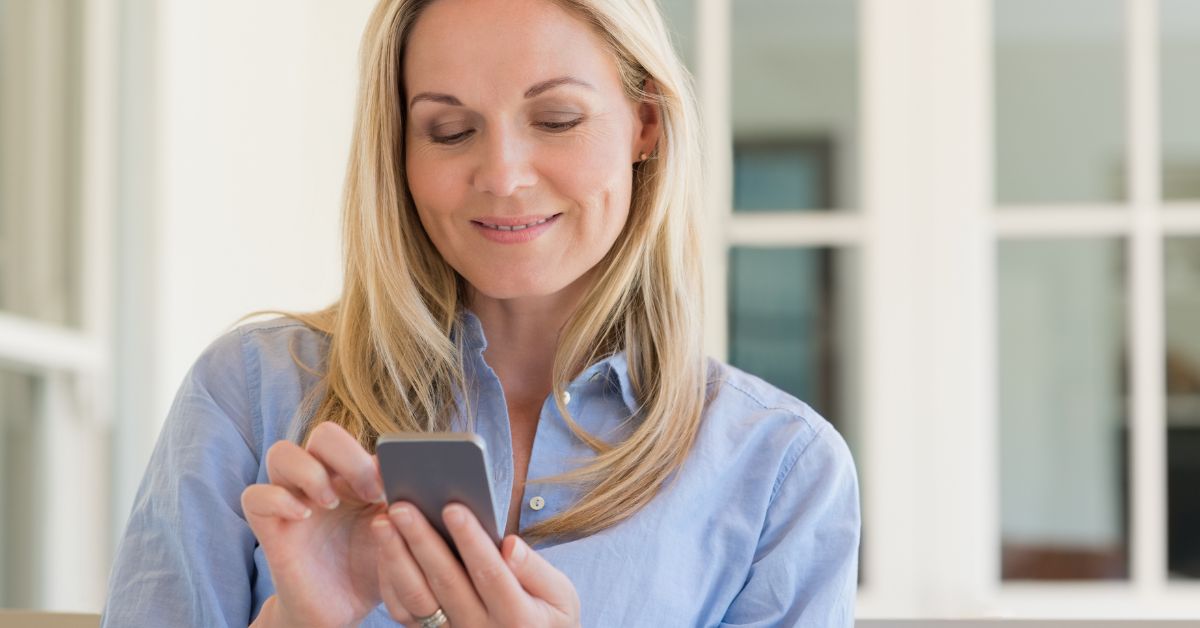 Smiling middle-aged woman using smartphone, representing safe online dating communication and connection for mature singles.