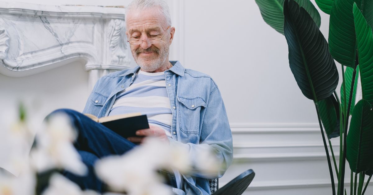 Older man enjoying a quiet moment reading a book at home, symbolizing self-care and personal growth after 50.