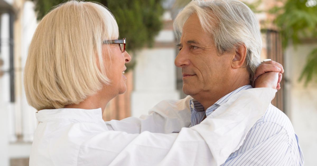 Smiling older couple embracing and looking into each other’s eyes outdoors, symbolizing trust, emotional intimacy, and healthy relationships.