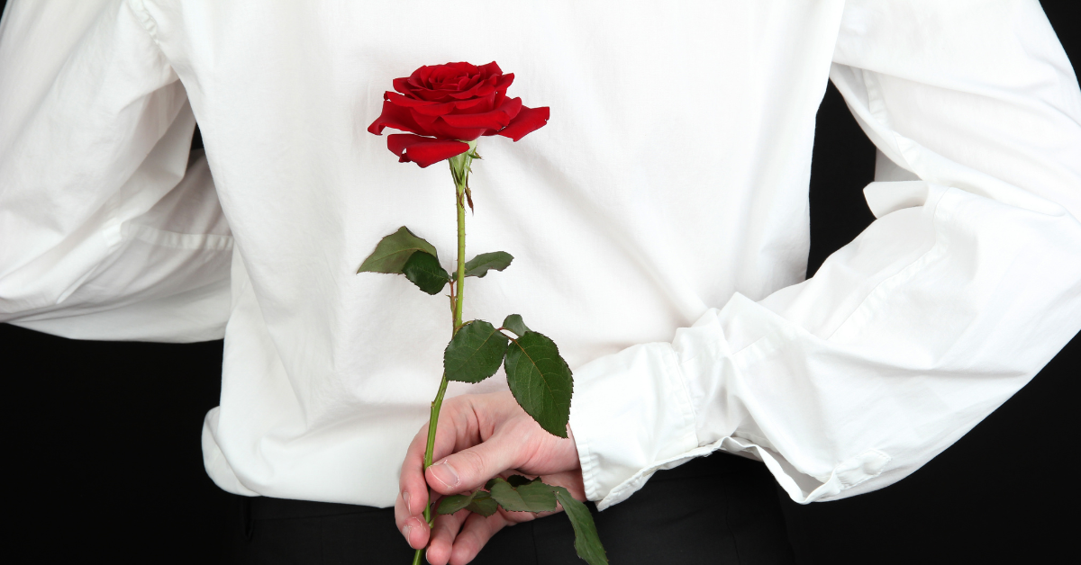 Man in white shirt holding red rose behind back for romantic surprise