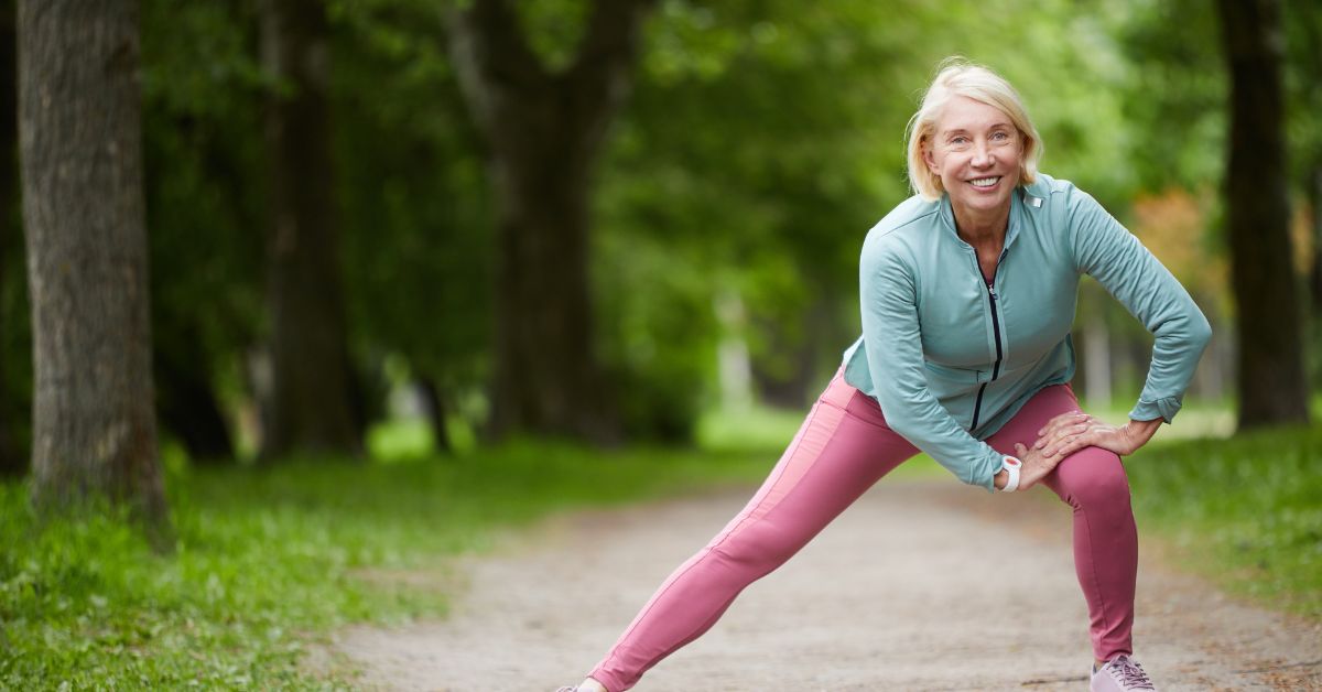 Older woman in athletic wear doing side lunges in a park, embracing fitness and wellness