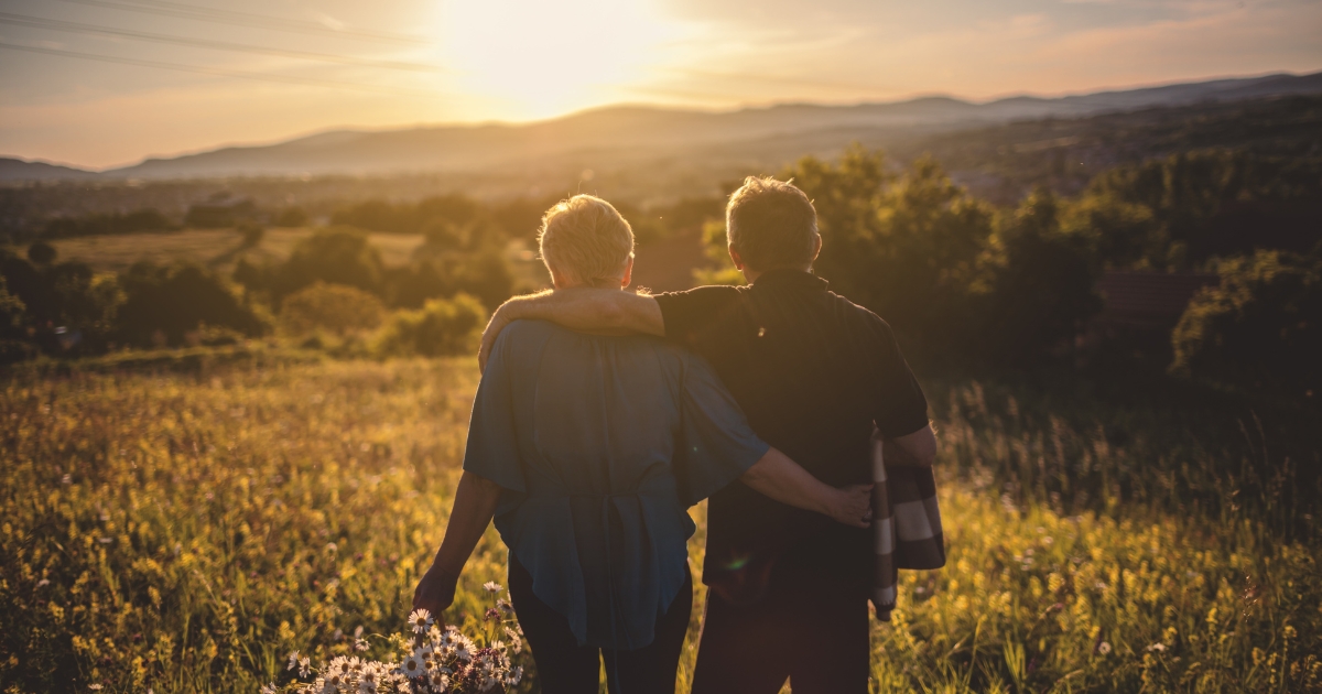 Love Lessons We Learn Later in Life - Mature Singles Finding Love Senior couple embracing while watching sunset in a field, symbolizing love after 50 and emotional connection.