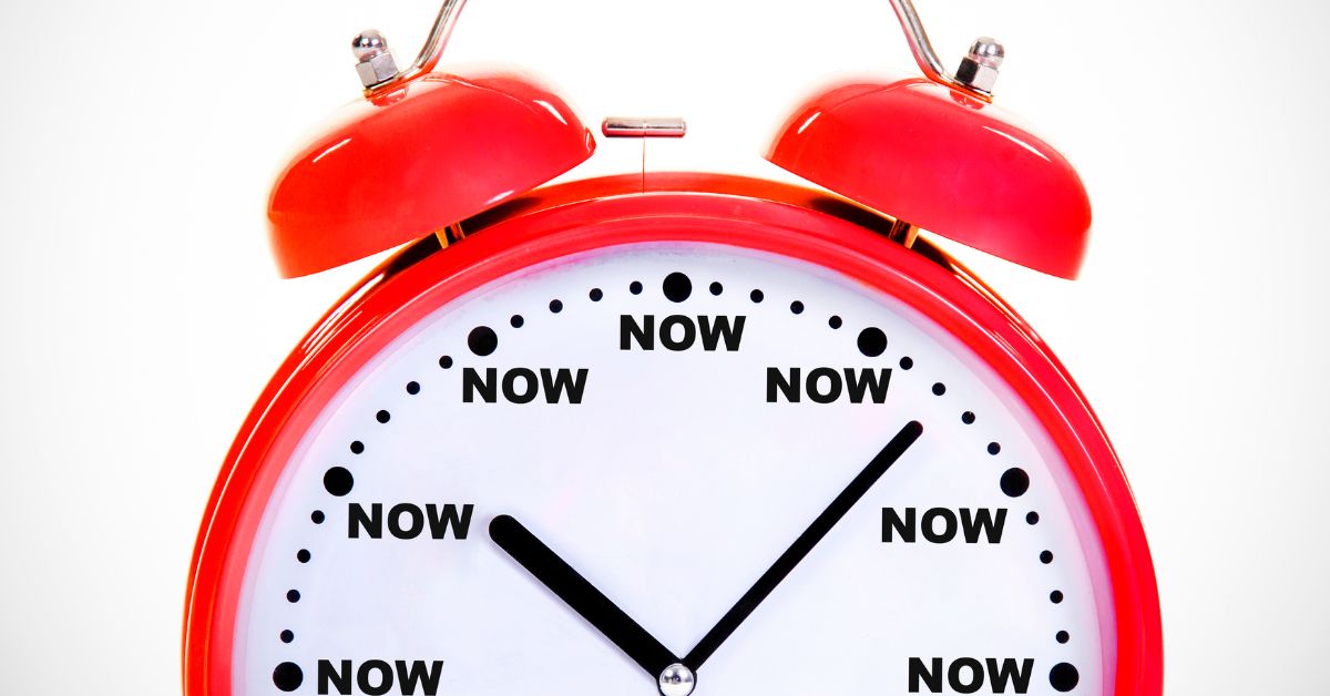 Moving In_ When Is It The Right Time - Mature Singles Finding Love Bright red alarm clock with the word "NOW" written at every hour mark, symbolizing urgency or the idea that the right time is now.