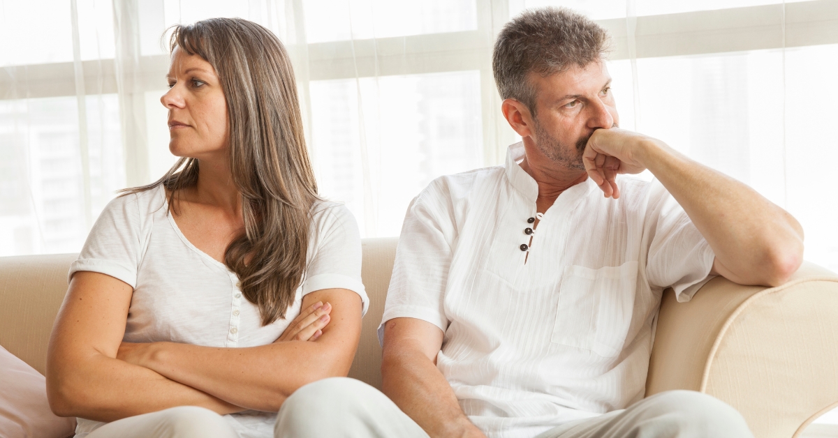 Overcoming Jealousy in Relationships - Mature Singles Finding Love Middle-aged couple sitting on a couch, looking away from each other with tense expressions, dealing with relationship conflict and jealousy.