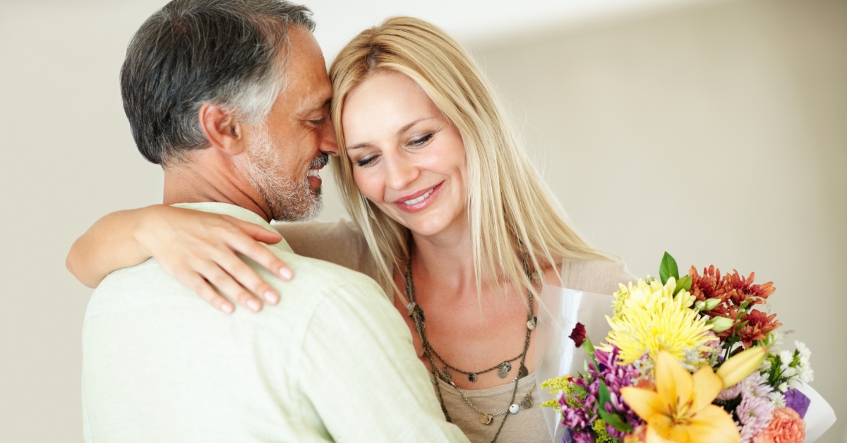 Physical Intimacy After 50_ Challenges and Joys - Mature Singles Finding Love Happy mature couple embracing with a bouquet of flowers, symbolizing love and connection after 50.