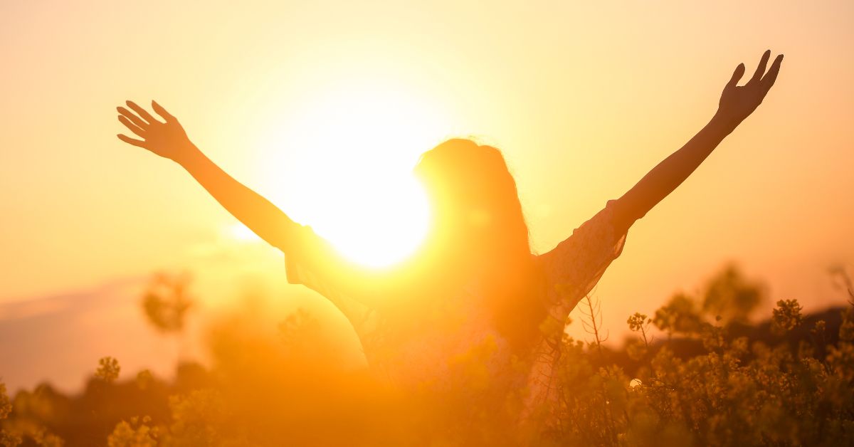 Silhouette of joyful woman in a field at sunrise, symbolizing empowerment and happiness after divorce.