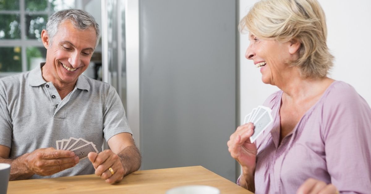 Happy senior couple playing cards and laughing together at home