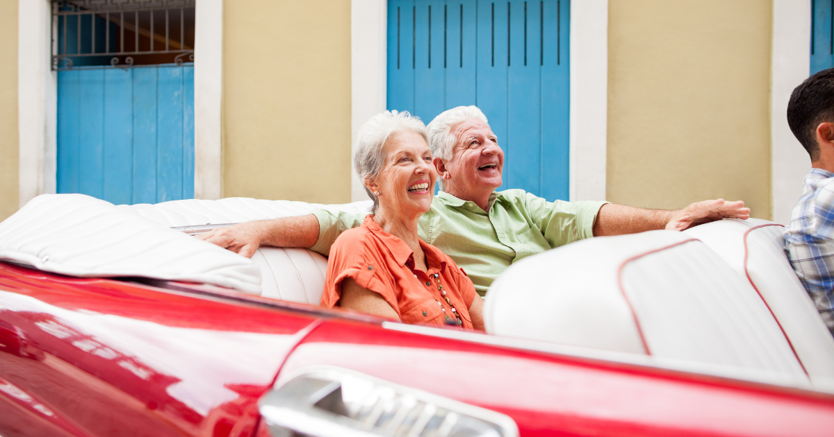 Rekindling the Spark_ Keeping Things Exciting In Your Mature Relationship - Mature Singles Finding Love An older couple smiling and enjoying a ride in a red convertible, showcasing joy and togetherness in a vibrant, sunny setting with colorful doors in the background.