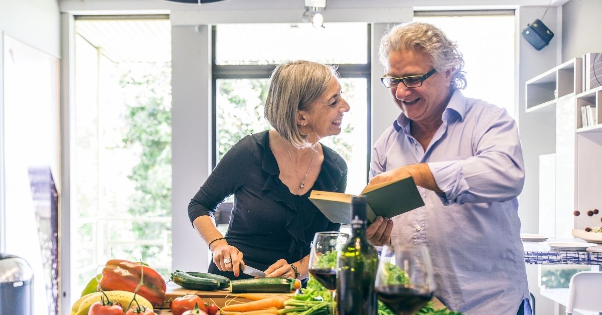 Happy mature couple cooking together in a bright kitchen, smiling and reading a recipe book – signs of emotional maturity and shared life moments
