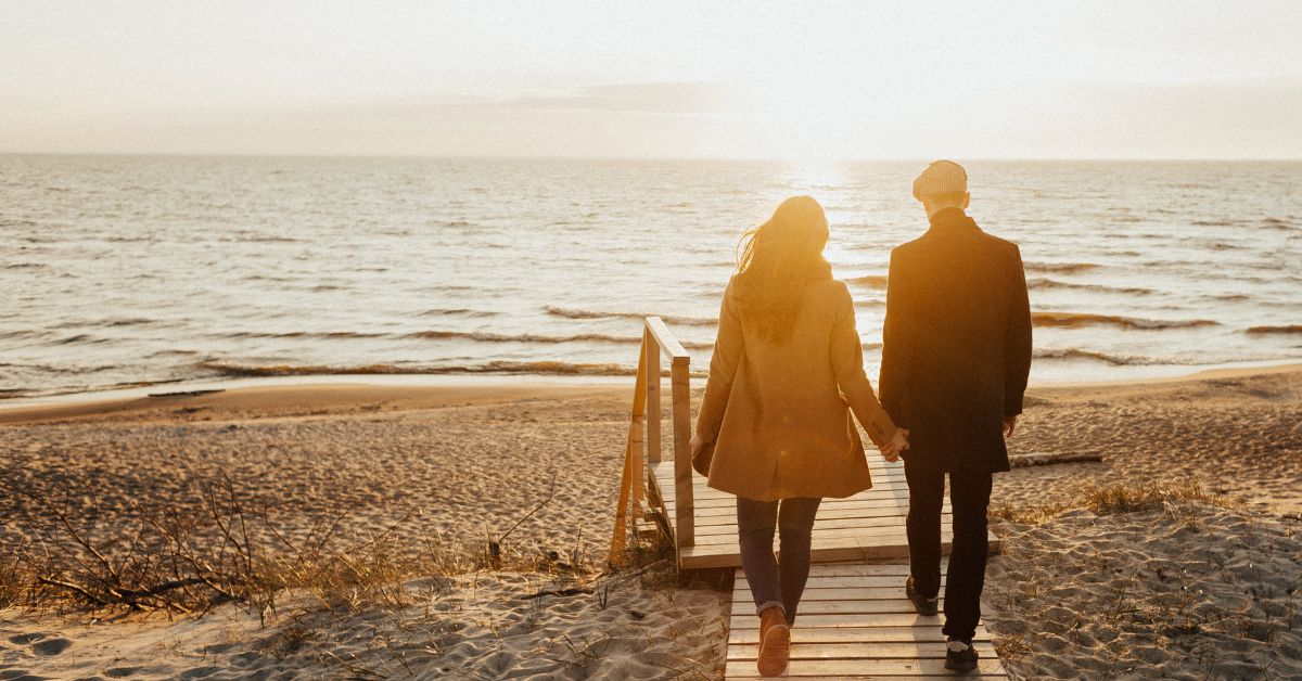 Couple walking hand in hand on a beach boardwalk at sunset, symbolizing healing, new beginnings, and rebuilding relationships after loss.