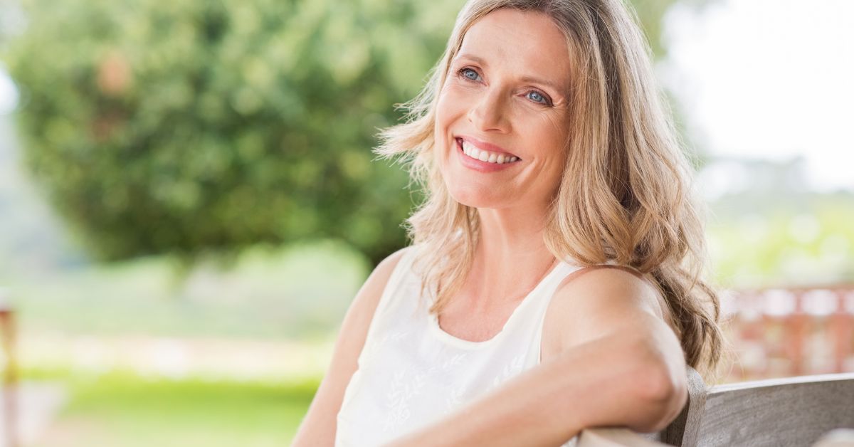 miling mature woman sitting outdoors, symbolizing confidence, peace, and empowerment after starting over post-divorce at 50.
