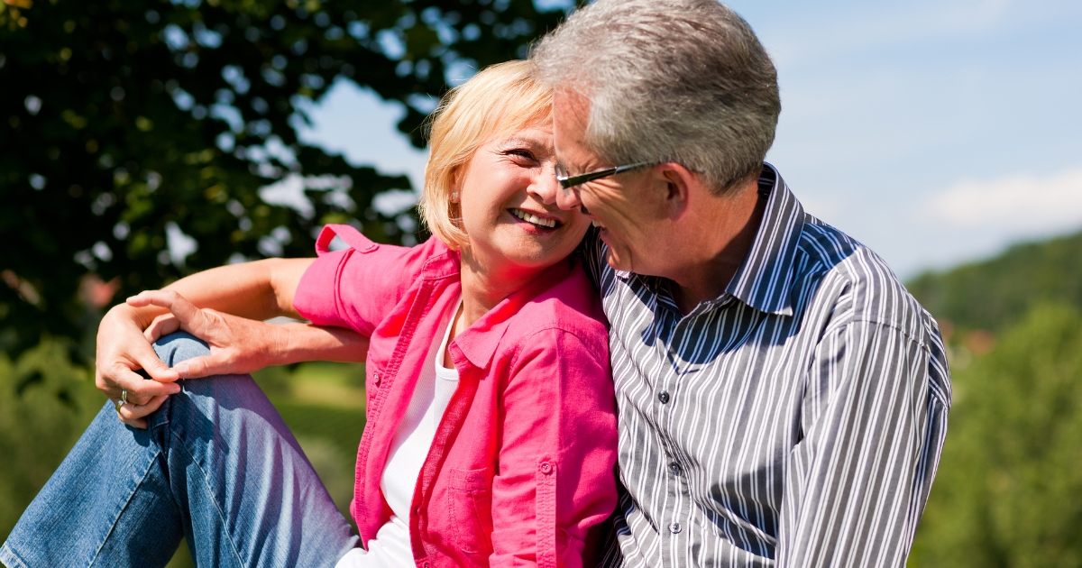 Smiling senior couple laughing and flirting outdoors on a sunny day, capturing the joy of dating and connection after 50.