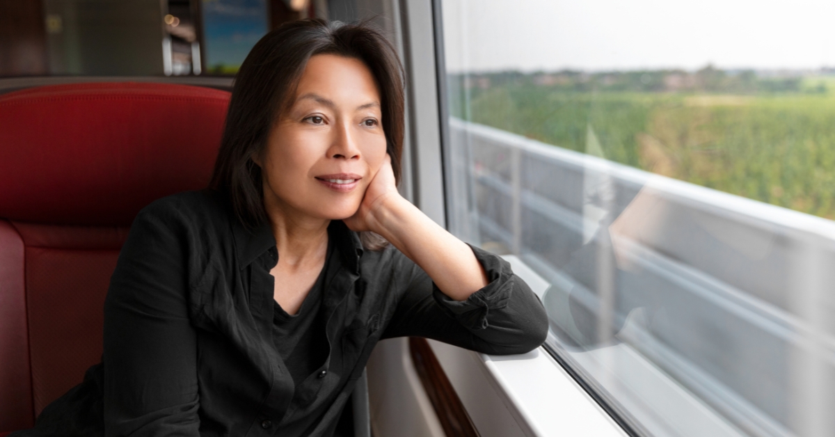The Benefits of Taking a Break from Dating - Mature Singles Finding Love Serene middle-aged woman gazing out of a train window, lost in thought and reflection. A peaceful moment of self-discovery and personal growth during a solo journey.
