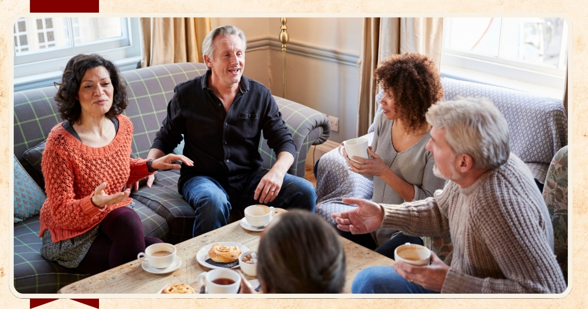 Group of middle-aged adults sitting in a cozy living room, chatting and laughing over coffee and pastries, illustrating friendship and social connection in later life.