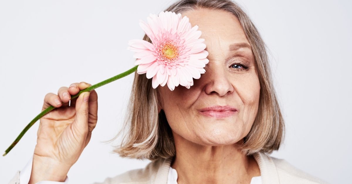 The Science of Desire_ Understanding Changes in Sexual Health Over 50 - Mature Singles Finding Love Mature woman smiling with a pink daisy, representing healthy aging and self-love