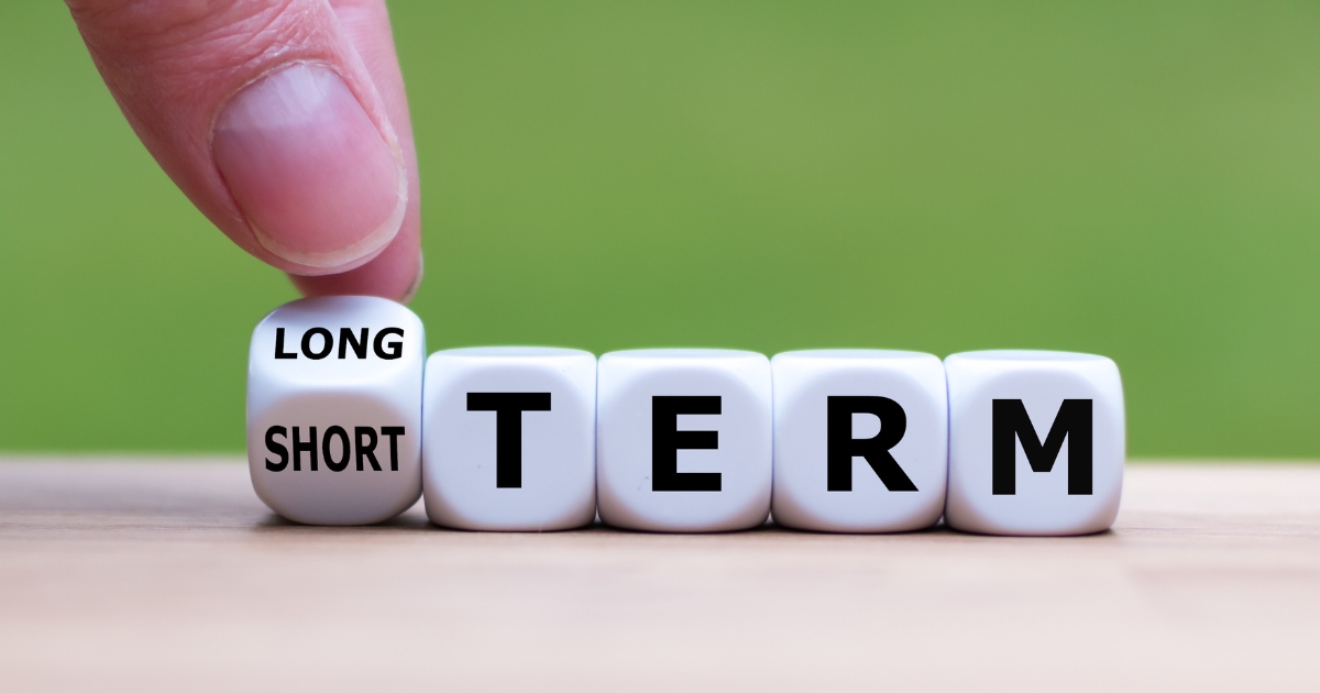 Tips for Talking About Long-Term Goals with a New Partner in Your 50s - Mature Singles Finding Love Hand flipping a dice between "short" and "long" next to the word "TERM," symbolizing the transition from short-term to long-term goals.