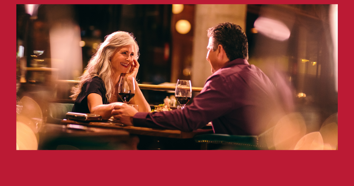 Understanding Modern Dating Etiquette for Seniors - Mature Singles Finding Love A senior couple enjoying a romantic dinner at a warmly lit restaurant, with glasses of red wine on the table and blurred lights in the background, creating a cozy ambiance.