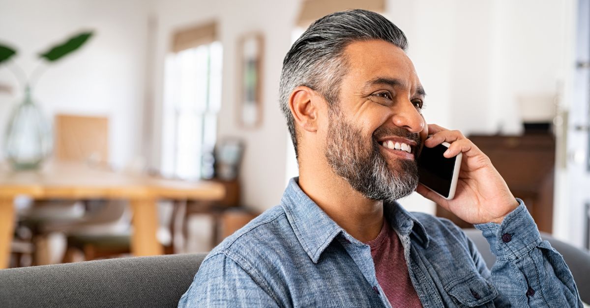 Smiling middle-aged man with salt-and-pepper hair talking on the phone at home – representing confident, emotionally available single men in their 50s.