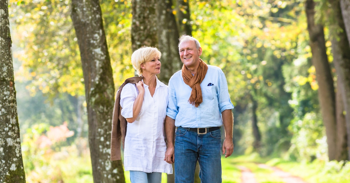 Why Its Never Too Late to Fall in Love Again - Mature Singles Finding Love Happy senior couple holding hands and walking through a scenic forest trail, symbolizing companionship, new beginnings, and love in later life.