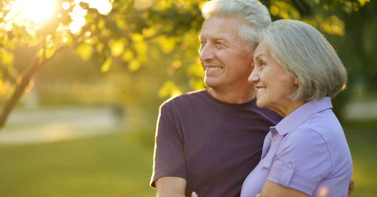 Happy senior couple embracing in a sunlit park, smiling and enjoying life together